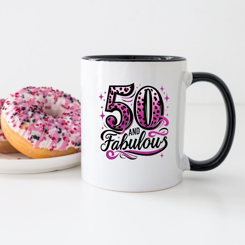 May include: White ceramic mug with a black rim and handle. The mug has a pink and black leopard print design with the text "50 and Fabulous".
