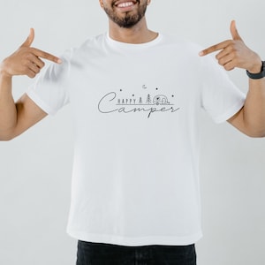May include: White t-shirt with a black graphic design that says "Happy Camper" with a camper, trees, and stars.