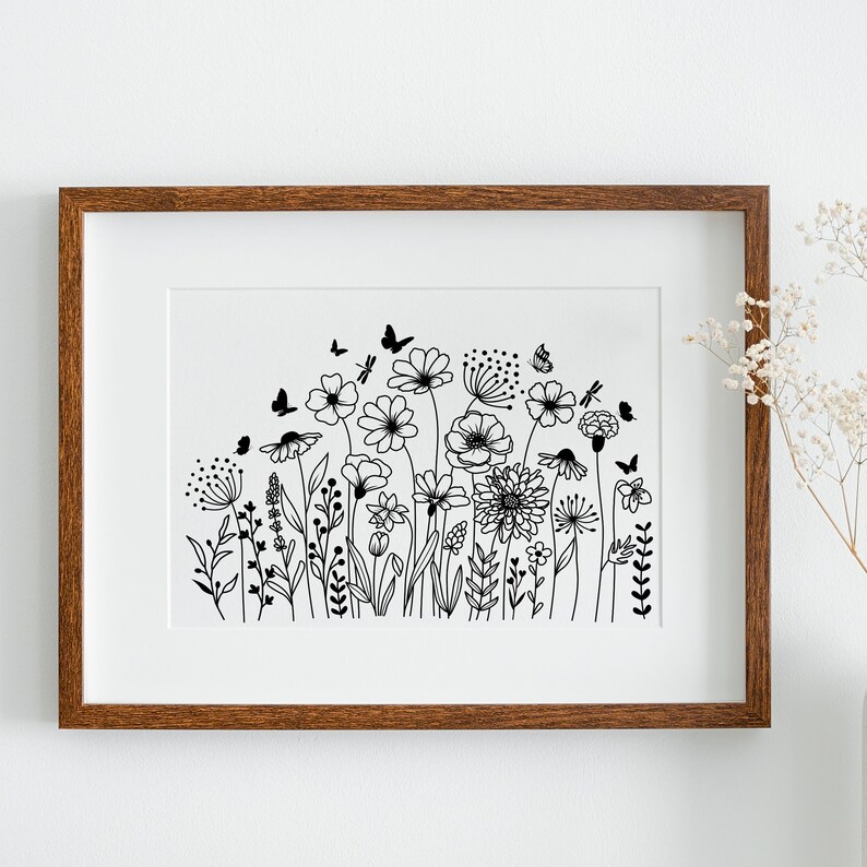 Op de afbeelding: Een zwart-witte lijntekening van een veld met wilde bloemen en vlinders. De tekening is ingelijst in een bruin houten lijst.