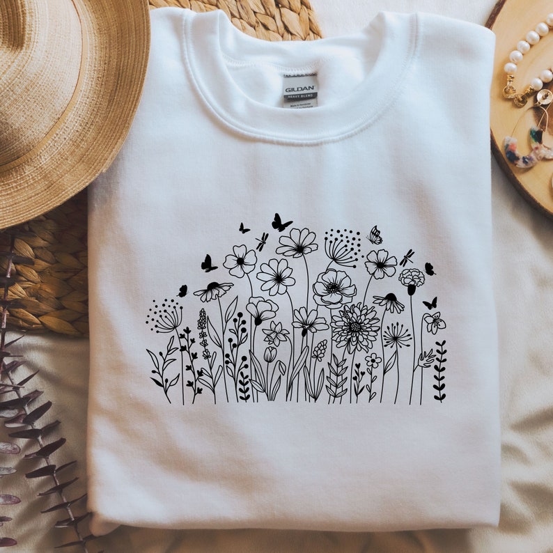 Op de afbeelding: Wit sweatshirt met een zwarte lijntekening van een bloemenveld met vlinders.