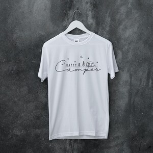 May include: White t-shirt with a black graphic design that says "Happy Camper" with a camper van, trees, stars, and a crescent moon.
