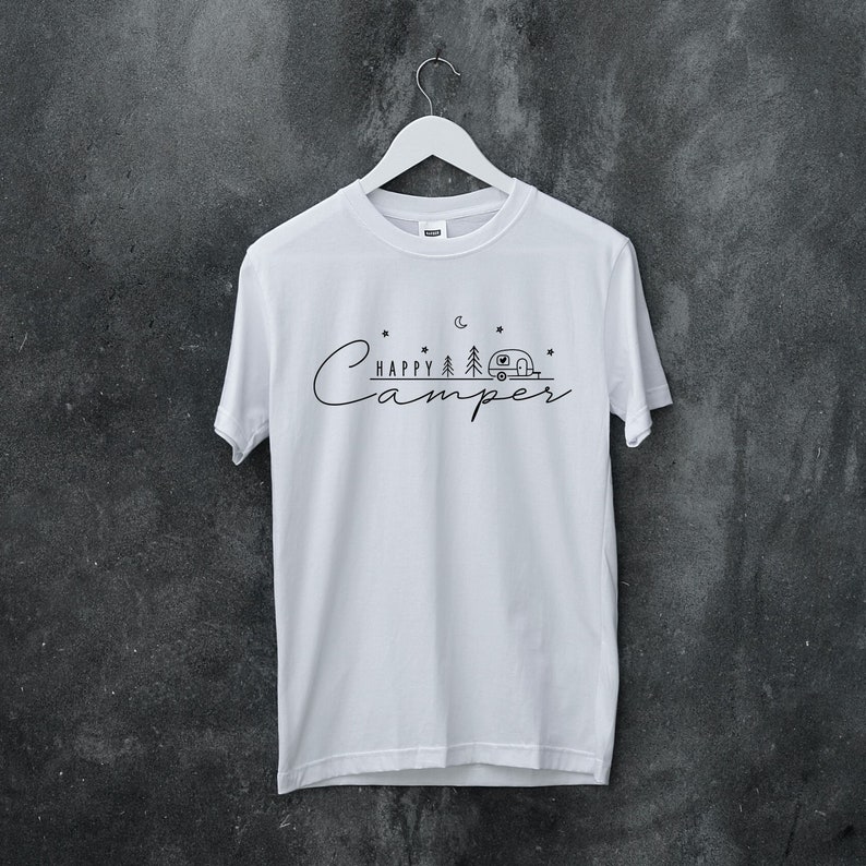 May include: White t-shirt with a black graphic design that says "Happy Camper" with a camper van, trees, stars, and a crescent moon.