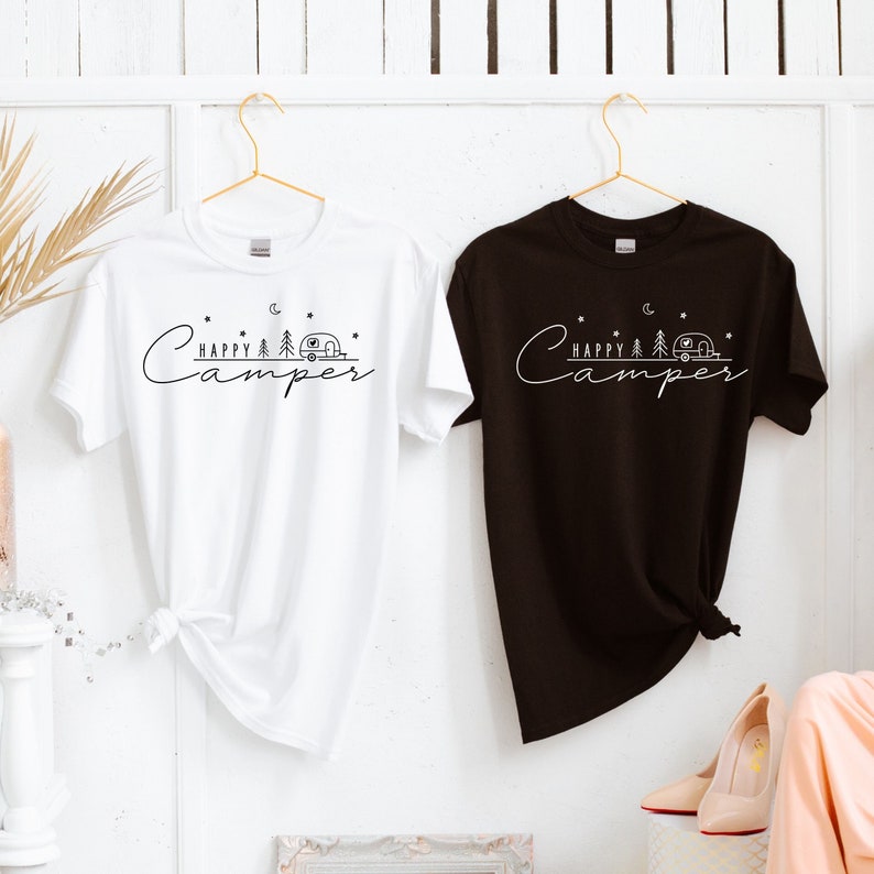 May include: Two t-shirts, one white and one black, with the text "Happy Camper" and a small camper van graphic. Both shirts are hanging on hangers.