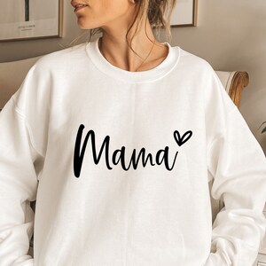 Może przedstawiać: Biała bluza z napisem "Mama" w czarnym, ozdobnym pismem i małym czarnym sercem.