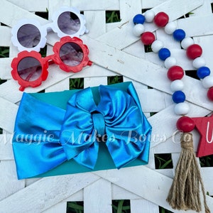 May include: A turquoise blue headband with a large bow, red and white flower-shaped sunglasses, and a red, white, and blue beaded garland with a wooden star that says "USA".