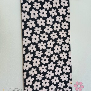 May include: Black fabric with a white floral pattern. The fabric is hanging on a wooden hanger.