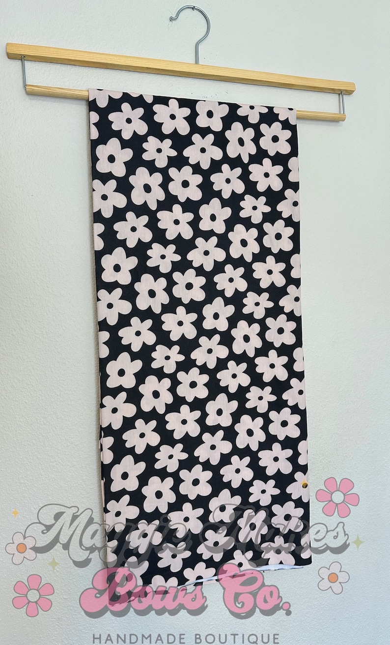 May include: Black fabric with a white floral pattern. The fabric is hanging on a wooden hanger.