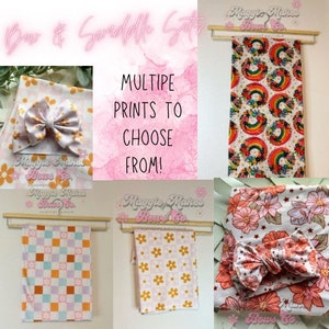 May include: A set of baby swaddles with different patterns, including a rainbow, floral, and checkered design. Each swaddle is paired with a matching bow. The text "Maggie Makes Bows Co." is visible on the image.