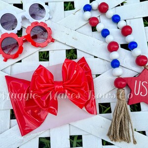 May include: Red, white, and blue beaded garland with a wooden star that says "USA" and a red patent leather bow.