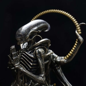 May include: A silver alien figurine with a gold halo, posed in a praying position. The alien has a translucent head and a detailed, segmented body.