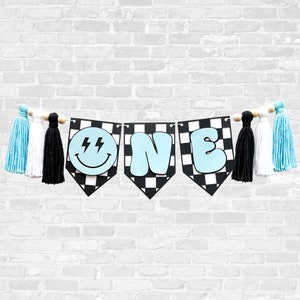 May include: A blue and black checkered banner with the word "ONE" in blue letters and a smiley face with lightning bolts. The banner is decorated with blue, white, and black tassels.