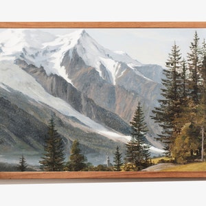May include: A framed painting depicting a snow-capped mountain range with a valley in the foreground. The mountain peaks are covered in white snow and the valley is filled with green trees. The painting is framed in a brown wooden frame.
