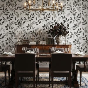 May include: A dining room with a dark wood table and chairs, set for a meal. The room features a floral wallpaper in black and white, a chandelier, and a buffet with decorative items.