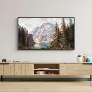 May include: A framed landscape painting depicting a mountain lake surrounded by trees and mountains. The lake is a light blue color and the mountains are a dark green color. The trees are a dark green color and the sky is a light blue color.