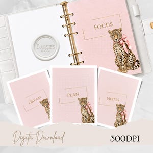 Könnte beinhalten: Ein weißer Ringplaner mit goldener Mechanik, der rosa Seiten mit Rasterlinien und goldenem Text mit den Wörtern Focus, Dream, Plan und Notes enthält. Jeder Abschnitt zeigt einen Leoparden mit einer rosa Schleife. Ein weißes Wachssiegel mit dem Text Darcie's & Co. ist zu sehen.
