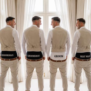 May include: Four individuals wearing white long-sleeve shirts, beige waistcoats, and beige trousers. The individuals are wearing underwear with text printed on the back waistband: two pairs read GROOMSMAN, one reads GROOM, and one reads BEST MAN.