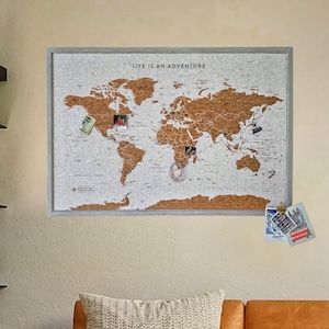 May include: A corkboard world map with a grey frame and the text "Life is an adventure" at the top. The map is covered in push pins and photos, indicating places visited.