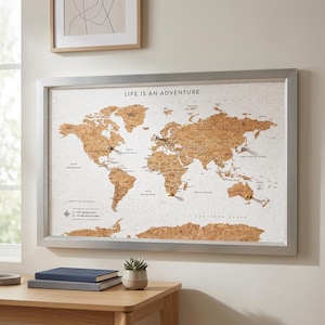 May include: A rectangular cork world map notice board framed in silver metal. The map features brown cork continents against a white background with the text LIFE IS AN ADVENTURE at the top. Several push pins are inserted into various locations.