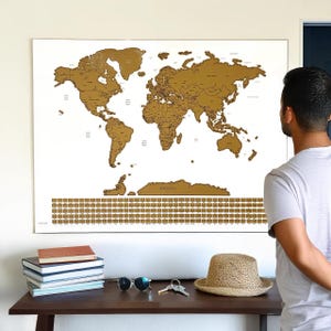 May include: A large rectangular scratch-off world map with a white background and gold-coloured continents. The map features detailed country outlines and a grid of small gold squares at the bottom for tracking travel destinations across the globe.