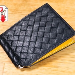 Puede incluir: Cartera con clip para billetes de cuero negro con un patrón tejido. El interior es amarillo. La cartera tiene un clip metálico y está sobre una superficie de madera. Un icono PDF está en la esquina superior izquierda.