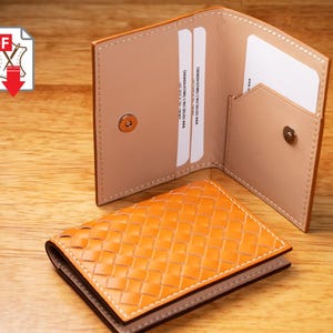 Op de afbeelding: Open leren portemonnee met een geweven oranje voorkant en een lichtbruin interieur. De portemonnee is open en onthult kaartsleuven en een klein vak. Een tweede, open portemonnee staat erachter. Op een houten oppervlak.
