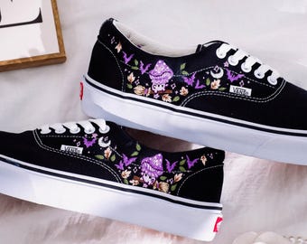 May include: Black canvas Vans sneakers with embroidered purple mushrooms, bats, and other Halloween-themed imagery. The shoes have white laces and a white sole.