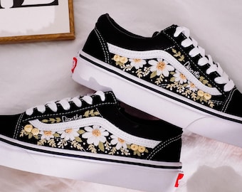 Peut inclure: Des baskets en toile noire avec des semelles blanches et des marguerites et des feuilles brodées en blanc. Le texte "Don't the" est brodé sur le côté de la chaussure.