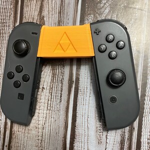 May include: A black Nintendo Switch Joy-Con controller with a custom orange and yellow 3D printed grip featuring a triangular design.