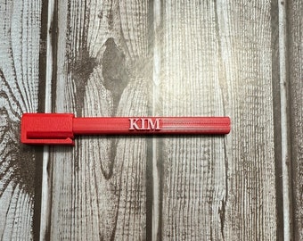Può includere: Una penna di plastica rossa con il nome "KIM" stampato su di essa.