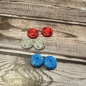Może przedstawiać: Sześć okrągłych, ozdobnych guzików w trzech kolorach: czerwonym, srebrnym i niebieskim. Guziki mają wypukły wzór i otwór w środku.