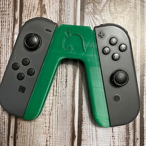 May include: Green and gray Nintendo Switch Joy-Con controllers with a green leaf design on the back. The controllers have buttons labeled A, B, X, Y, +, and -.