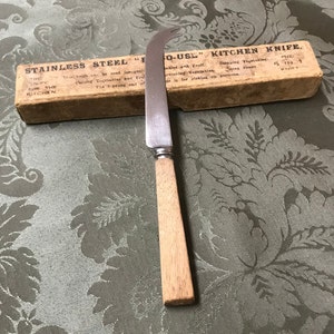 May include: A stainless steel kitchen knife with a wooden handle. The knife is in its original packaging, which reads "Stainless Steel "F" O-US" Kitchen Knife. The 5 in 1 Kitchen Knife is for slicing vegetables, fruits, and for picking up portions."