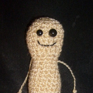 May include: A crocheted peanut-shaped toy with a smiling face and black eyes. The toy has long, thin arms and legs.
