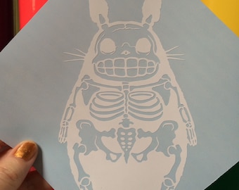 May include: White vinyl decal of a cartoon character, Totoro, with a skeleton design. The character is standing with its arms at its sides and has a large, round belly.