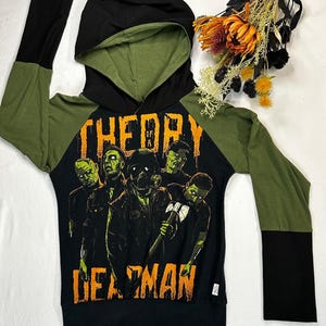Peut inclure: Sweat-shirt à capuche à manches longues noir et vert avec un imprimé graphique d'un groupe de zombies avec le texte "The Day of a Dead Man".