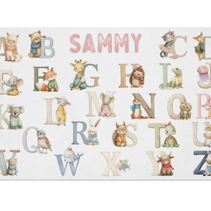 May include: A rectangular white mat featuring the alphabet with watercolor illustrations of animals. Each letter has a corresponding animal, such as a bear for B and a koala for K. The name "SAMMY" is written in pink letters above the alphabet.