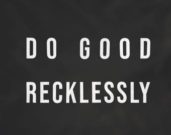 May include: A rectangular black flag featuring the white text DO GOOD RECKLESSLY centered in a bold sans-serif font. The flag includes small metal grommets in the top and bottom left corners for hanging, displaying a clean and simple design.