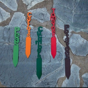 Può includere: Cinque segnalibri da giardino in legno con i nomi di diverse verdure scritti su di essi. I segnalibri sono dipinti in diversi colori: verde, arancione, verde scuro, rosso e marrone.