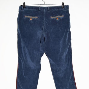 Op de afbeelding: Een blauwe corduroy broek met rode en grijze strepen aan de zijkanten. De broek heeft een gezoomde zoom en twee achterzakken.