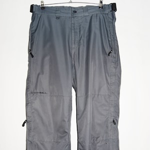 May include: Grey O'Neill ski trousers with a black belt and zipped pockets. The trousers have a relaxed fit, designed for winter sports. The O'Neill logo is visible on the left leg. The trousers are hanging on a metal hanger.