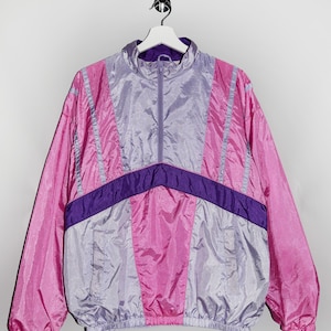 Peut inclure: Une veste coupe-vent rose et violette avec une fermeture éclair. La veste a un design géométrique avec des panneaux de couleurs contrastées.