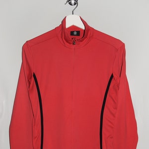 May include: A red long-sleeved shirt with black trim on the sleeves and sides. The shirt has a mock neck and a zip closure.