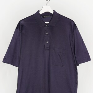 Op de afbeelding: Een donkerblauw, kort mouwig poloshirt met een enkele borstzak en een knoopsluiting. Het shirt heeft een merklabel met de tekst "Guy Laroche" op de achterkant van de kraag.