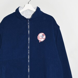 May include: A navy blue fleece jacket with a white zipper and a New York Yankees logo on the front. The jacket is reversible and has a white fleece lining.