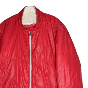 May include: A red puffer jacket with a white zipper and a white lining. The jacket has a stand-up collar and a drawstring at the waist.