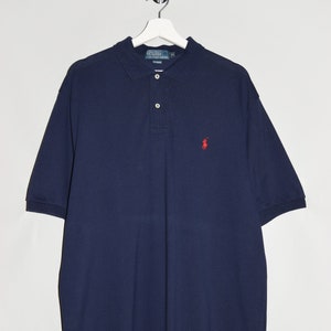 Puede incluir: Una camiseta polo azul marino con un pequeño logo bordado de jugador de polo rojo en el pecho izquierdo.