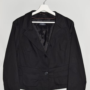 Puede incluir: Una chaqueta negra con un cierre de botón único y dos bolsillos. La chaqueta tiene una etiqueta que dice "Daniel Hechter Paris".