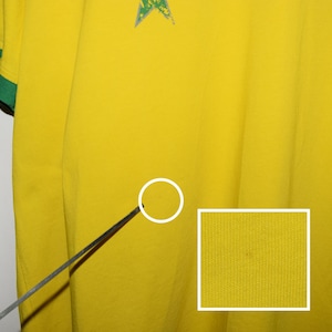 May include: Close-up of a yellow fabric with a textured surface. The fabric has a small, dark spot.