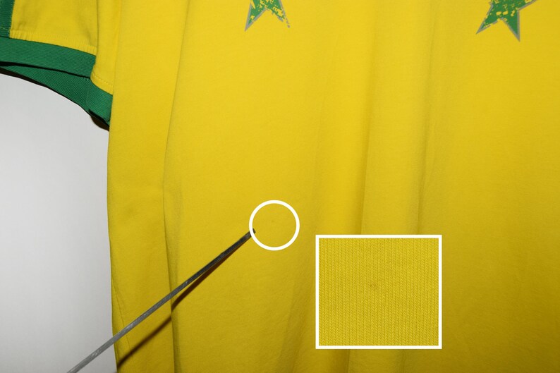 May include: Close-up of a yellow fabric with a textured surface. The fabric has a small, dark spot.