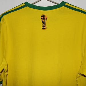 May include: Yellow short-sleeved t-shirt with green trim and a small graphic of a soccer trophy on the back.
